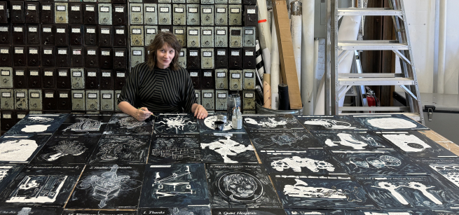 artist ellen harvey in front of a table of her artwork