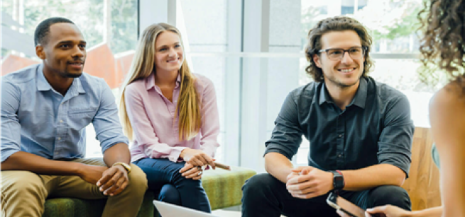 A group of adults listen to one another speak while seated around a table.