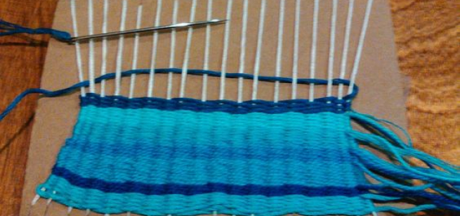 a half finished woven design on a cardboard loom