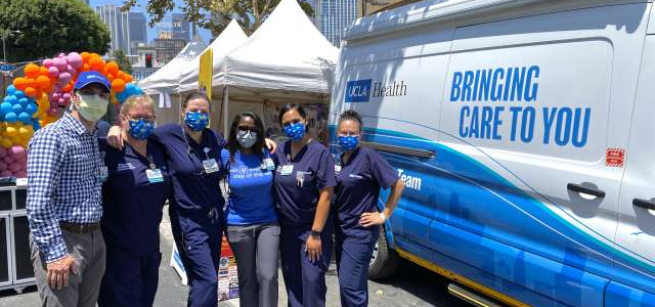 several healthcare workers in blue scrubs standing by a blue and white van that says UCLA Health bringing care to you along the side