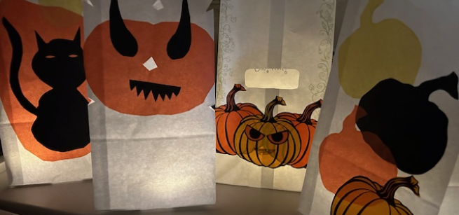 Four white luminaria paper bags decorated with Halloween themed cutouts such as orange, black, and yellow evil pumpkins.