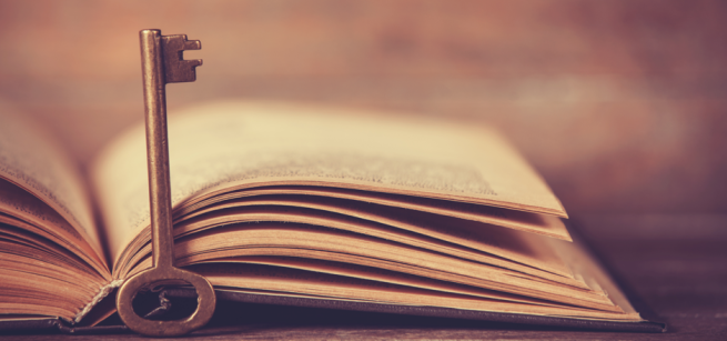 old-fashioned key standing next to an open book in sepia tones