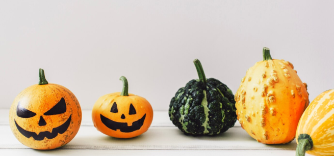 two mini pumpkins with jack-o-lanern faces, one green gourd, and two yellow-orange gourds