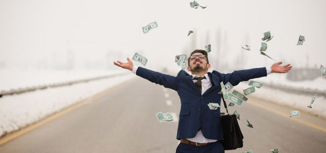 Young adult man in blue suit with briefcase standing in the center of the highway with cash falling on him from above