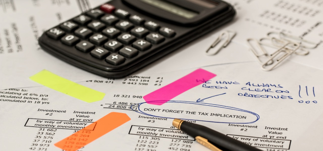 a black calculator on top of business papers with bright neon post it notes and a pen