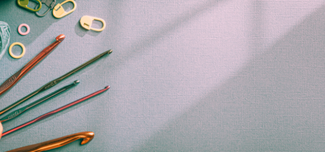 spools of yarn, five different sized crochet needles and crochet markers on a table