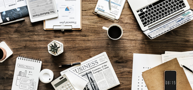 two coffee cups, one phone, one laptop and several notebooks and papers on the table
