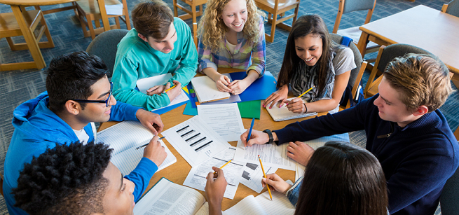 Group of high schoolers smiling while looking at papers scattered around the table.