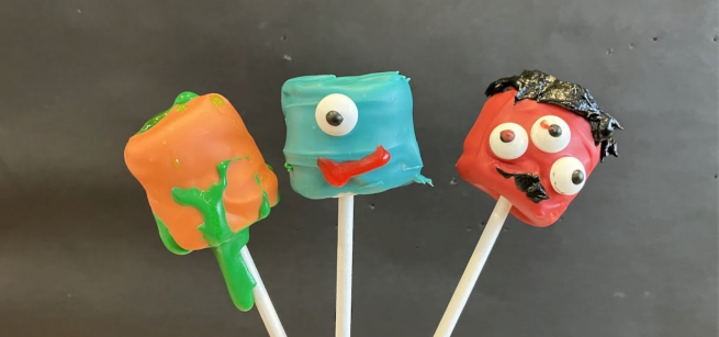 Three candy coated and decorated marshmallows: orange, blue, and red