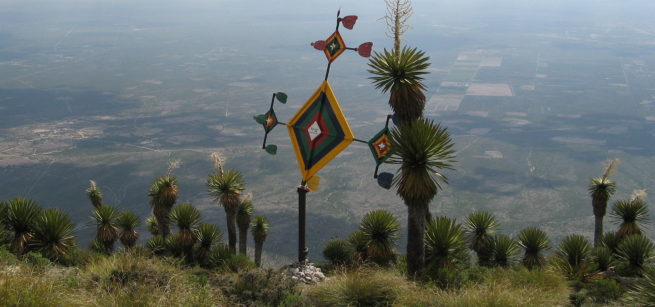 Ojo de dios on hill surrounded by dessert plants overlooking town below