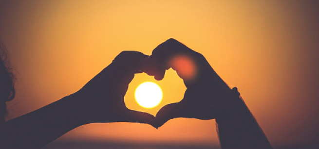 hands in shadow making a heart symbol around a bright sun 