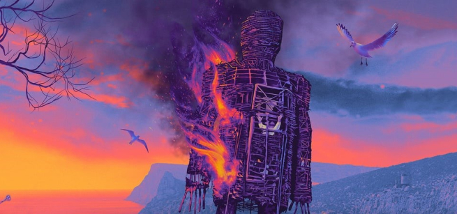 A still from the film "The Wicker Man" depicts a wooden statute of a man burns against a sunset, surrounded by sea gulls. 
