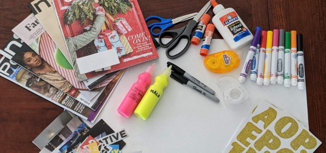 White poster board surrounded by colored pens, glue, a pile of magazines and words cut out of magazines