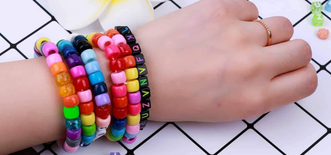 white hand with multiple multi-colored beaded bracelets on the wrist