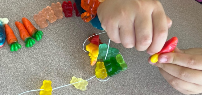A pair of hands creating stringed colorful candy jewelry