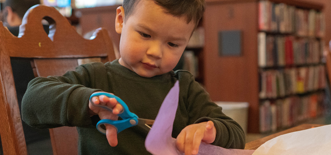 Child cutting purple paper for craft