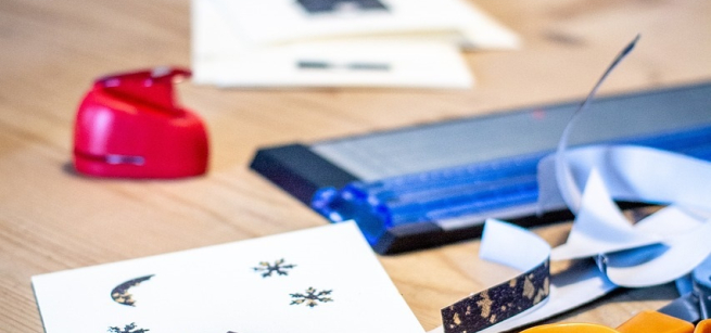 Holiday card, wrapping paper, and card making tools including stamper, scissors, and a paper cutter.