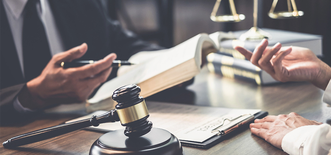 a gavel on a desk and two sets of hands with one holding an open book