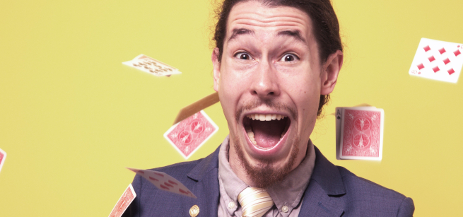 Head & shoulders of white male in suit, big grin, with playing cards in air