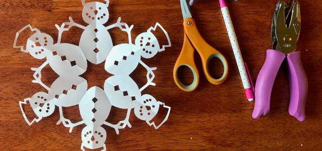 paper snowflake made out of different cut out snowmans with scissors and a hole punch