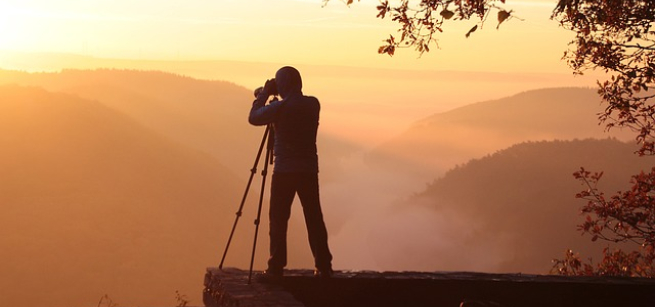 person at a viewpoint looking through camera at sunset