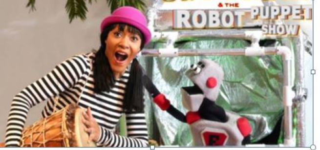 Woman beating conga drum standing next to robot puppet.