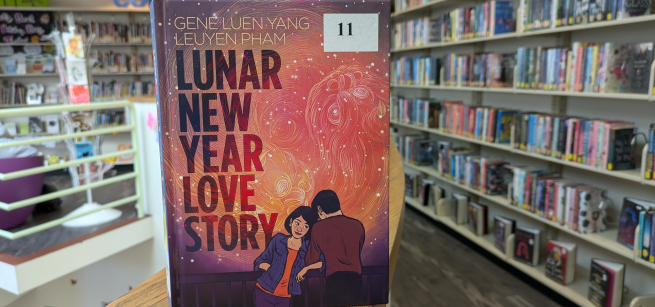 Image of library stacks and close up of book with two people and red and orange colors on the cover. 