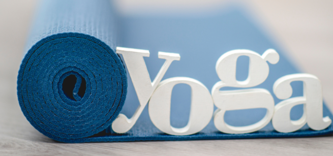 a blue yoga mat is slightly unfolded with a clay figurine spelling out the word yoga on it resting on the mat
