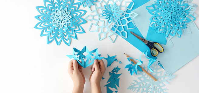 small hands holding a paper cut out of a snowflake 