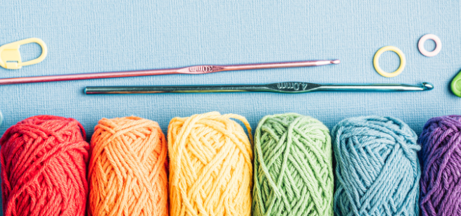 Six balls of yarn of various colors with two crochet needles on a blue background