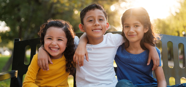 three smiling children on a bench