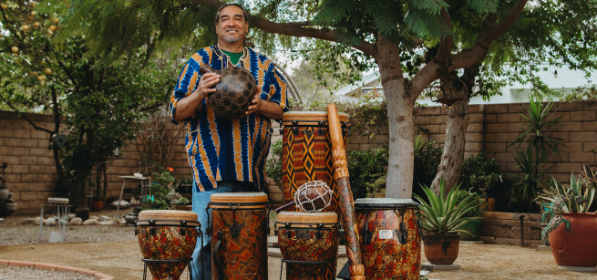 Man standing with 6 different African drums and percussion instruments