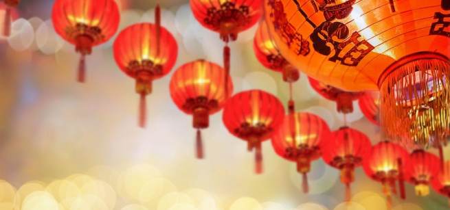 A row of red lanterns hang above with yellow lights in the distance. 