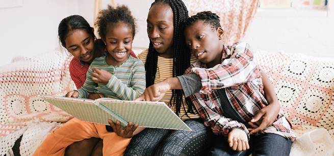 A woman and three children sit on a sofa and read a book together.