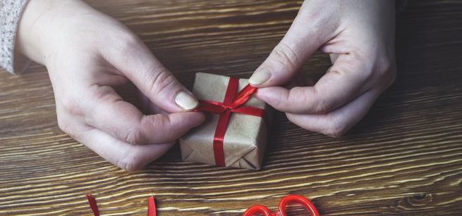 Two hands tying a red ribbon around a small box