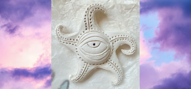 Image depicts a white clay sculpture in the stylized star formation with an eye in the center, over a background of a sunset.