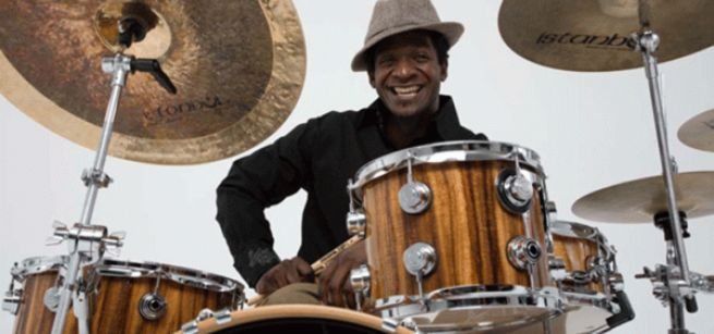 A smiling man sitting behind a drum set. 