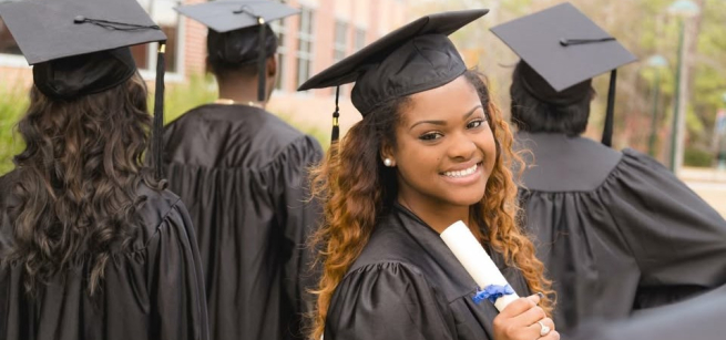 Female student smiling, wearing a cap and gown, and holding her diploma.