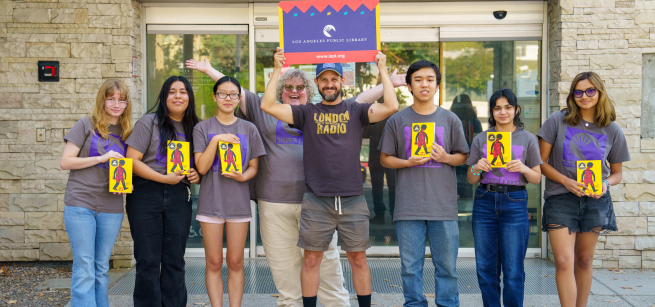 Holding bright yellow copies of Free Lunch, several teens and a librarian wearing volunteer t-shirts stand in front of the Silver Lake Library with the book's author, Rex Ogle, holding a large LAPL Library Card over his head.