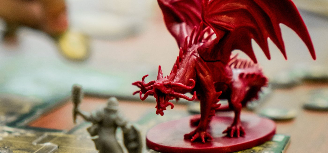 Red dragon game piece in the middle of a board game and hand holding a gold piece in the upper left corner