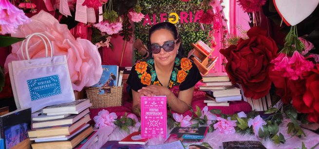Ariadna Sánchez Hernández holding her book Visitas inesperadas, surrounded by flowers and books