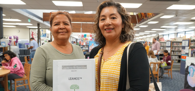 Two smiling women holding reading workbook.