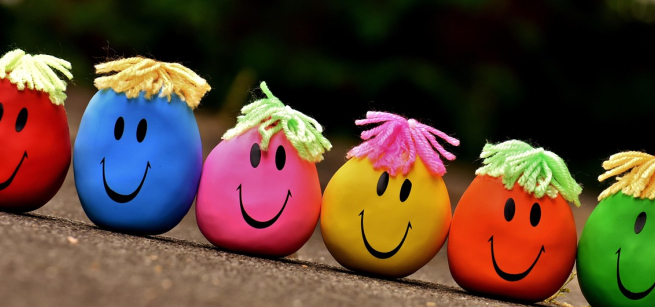 a row of colorful round balls with smiley faces and yarn for hair.