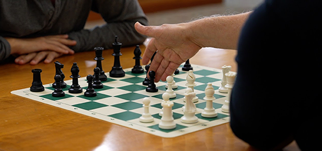 Two chess players, one moving a pawn on the chess board