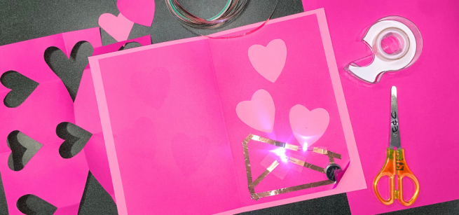 pink paper with cut out hearts and a pair of scissors and tape