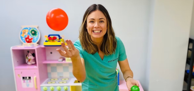 A smiling woman throws a ball in the air. She is surrounded by toys for children