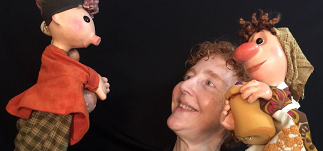 Woman holding up and looking at two puppets.