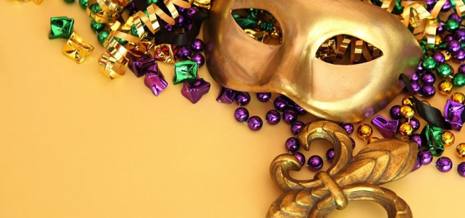 a gold mask lays on a background of green gold and purple mardi gras beads
