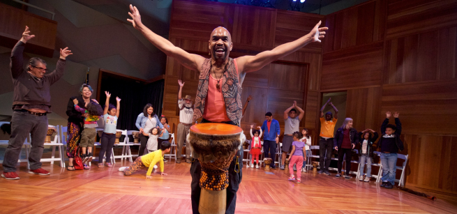 Chazz Ross with djembe drum in front of drum circle participants