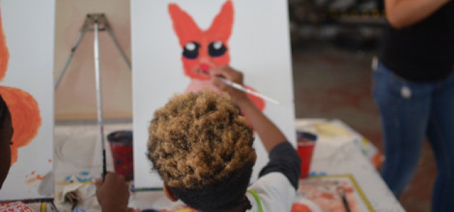 Child facing a canvas paints a red rabbit.
